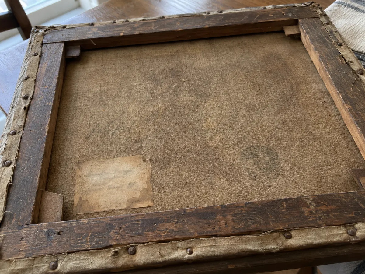 The back of an old canvas: dark wooden stretcher bars, rusty tacks, a faded paper label, an ink stamp and a pencil note